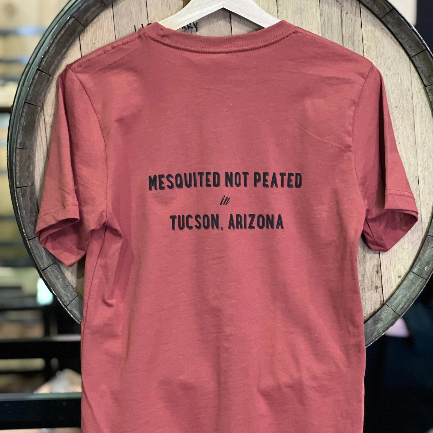The back of the Whiskey Del Bac t-shirt that says mesquited not peated in Tucson, Arizona. 